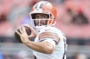 Joe Flacco, wearing a white jersey and orange helmet, stands with his arms raised mid-throw.