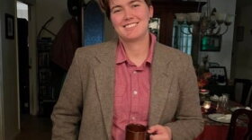 KERA News reporter Kailey Broussard poses in a green tweed suit, red button-down shirt holding a brown coffee mug.