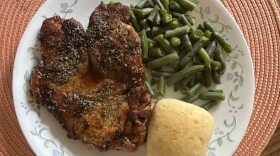A plate with a pork chop, dinner roll and green beans is sitting on an orange placemat.