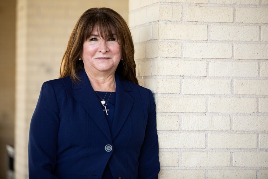 Stephanie Elizalde wears a blue jacket and stands next to a white brick wall. 