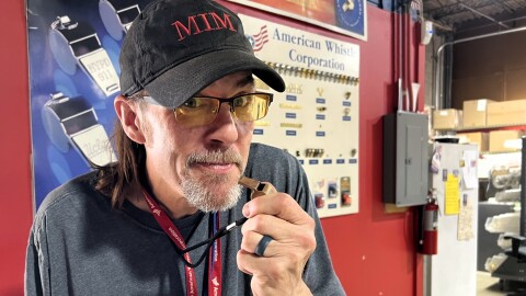 Phil Clark holds a metal whistle to his mouth. The wall behind him is covered in posters featuring the instrument.