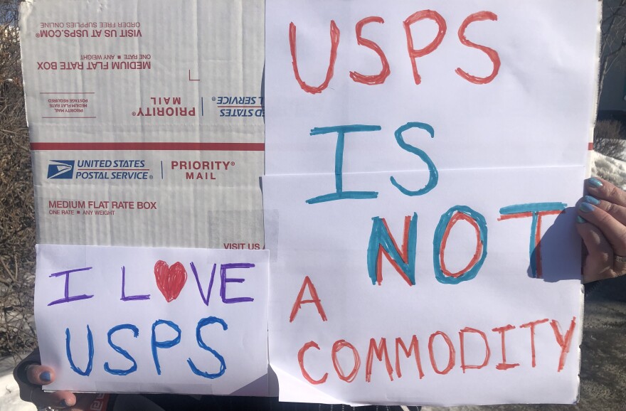 A protester holds a sign in front of the Downtown Fairbanks post office on Thursday, March 20.