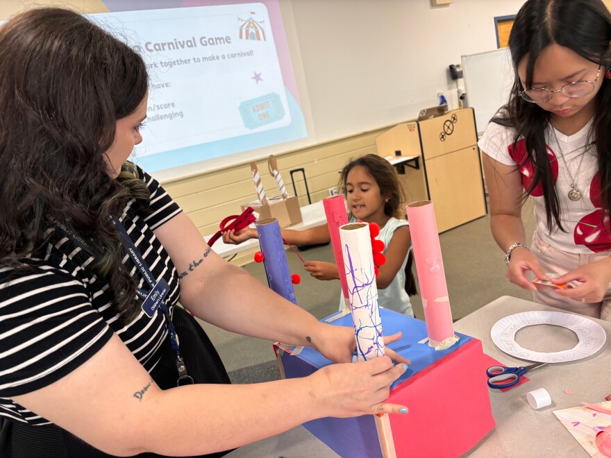 Intern Julia Rose Palad and Emily Woodbury, a Children's Librarian at Warwick Public Library, work with a student on her carnival game.