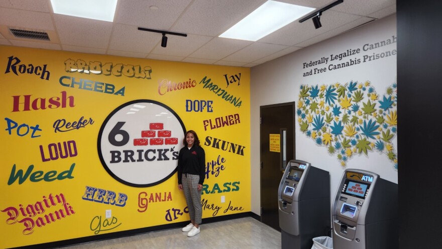 Payton Shubrick, founder of 6Brick's, a cannabis retailer in Springfield, Massachusetts, in front of the word cloud wall that is one of several references to the history of marijuana inside the store.