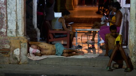 A man sleeps in the doorway of his home while others pass the time trying to cool off in the street in Havana, Cuba, Tuesday, Aug. 4, 2026.