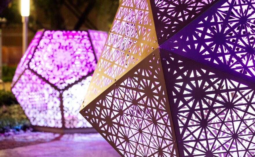 A close-up of two geometric shapes illuminated from the inside in a park at night.