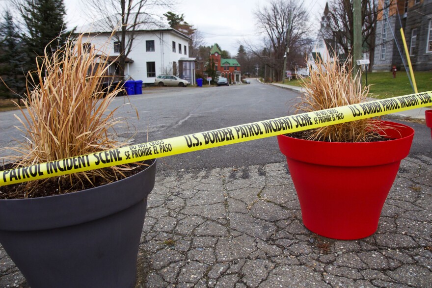 Yellow tape reading u.s. border patrol incident scene running across red and black flower pots in a street