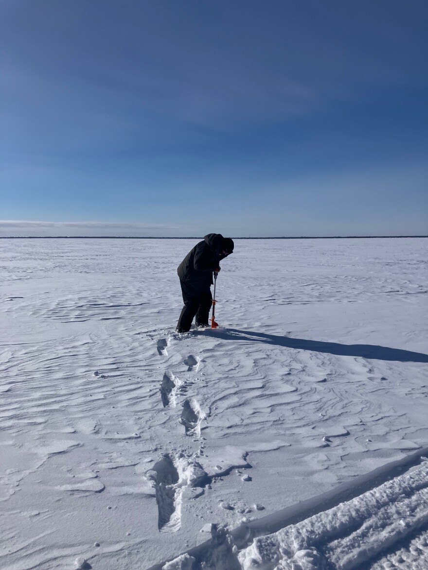 A person with an ice auger prepares to drill into a frozen lake