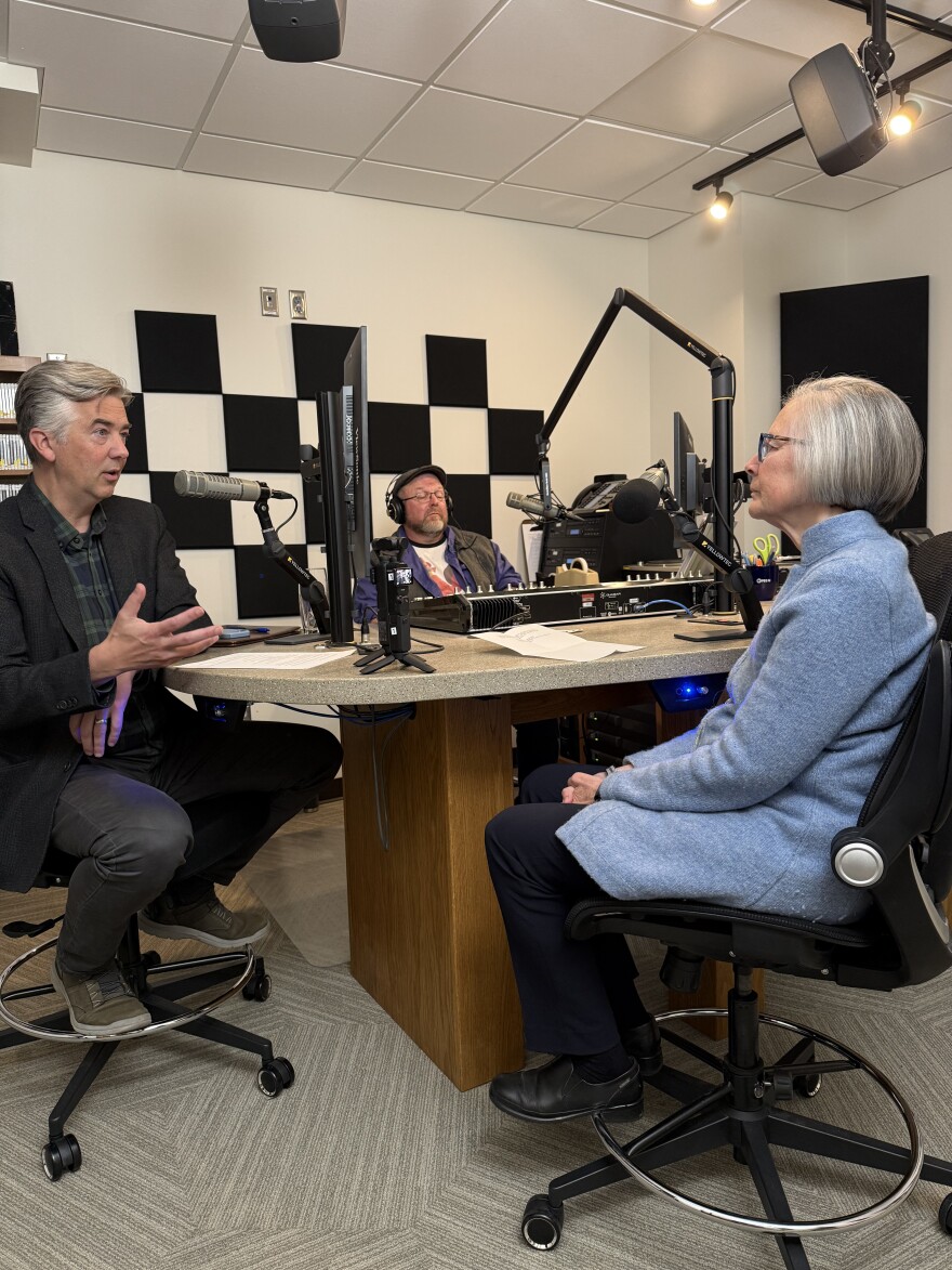 Three people sitting in a radio studio speaking into microphones