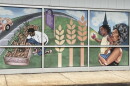 A mural on the outside of the Feeding America Eastern Wisconsin building in Milwaukee depicts a scene of a man tending to crops at the nearby Alice's Garden, and a woman carrying a child who's holding an apple