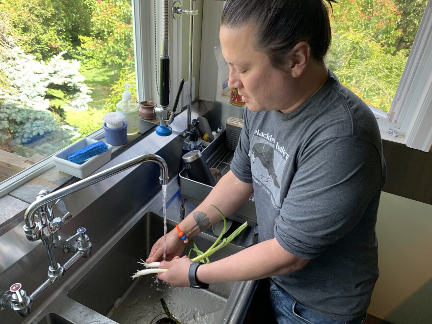 J. Kenji López-Alt, in a Blackbird Bakery t-shirt, washing onions at a sink with picture windows in the background