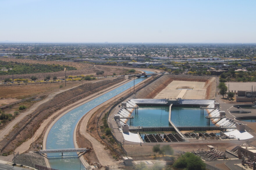 water flows through a canal next to two large industrial pools with a suburb in the background