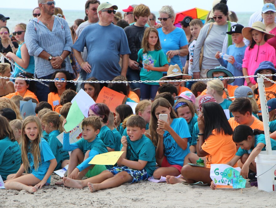 Summer campers at the Loggerhead Marinelife Center wait to see a loggerhead turtle released, waving signs that say "Welcome Home!" and "Good Luck Bovenizer"