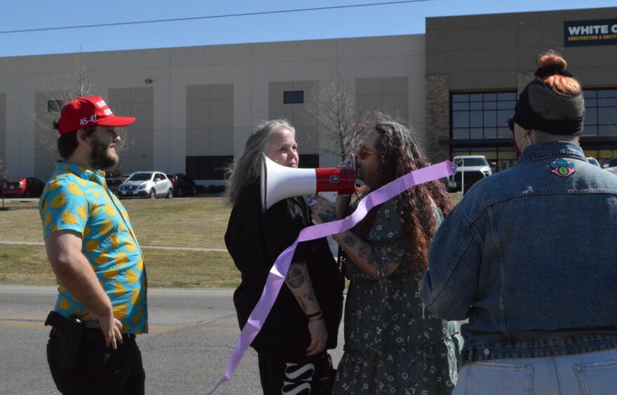 A Trump supporter carrying a pistol who only gave his name as Eric stands in front of Trump protestor Carrie Ford as she speaks through a bullhorn on Saturday, March 22, 2025.