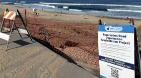 The desalination project by Marina Coast Water District is in its first phase, which involves cleaning an existing beach intake well at the Marina State Beach. A blue and white sign is at the front of the site marked by red cable wire. An orange and white construction sign is next to it.