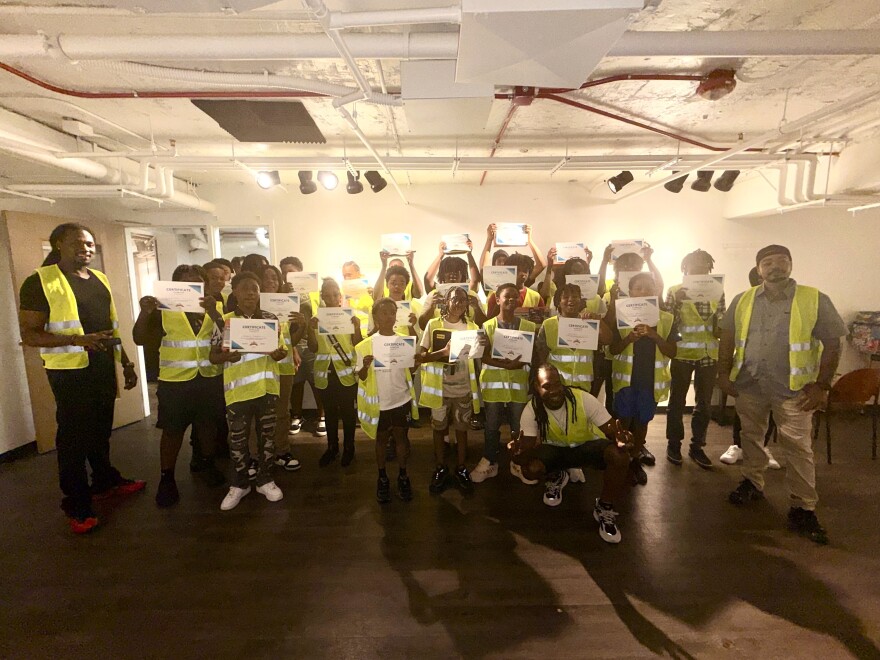 About 18 Handyman Academy graduates wearing yellow reflective safety vests pose together for a group photo.