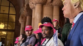 Food service workers from across New York joined lawmakers at the statehouse Monday, Jan. 27, 2025, to push for a bill that would nix the “subminimum wage” that workers currently receive, and require employers pay the full minimum wage on top of tips. An organizer from labor rights group One Fair Wage wore a mask of President Donald Trump to criticize his alleged support of large corporations that poorly treat service workers.