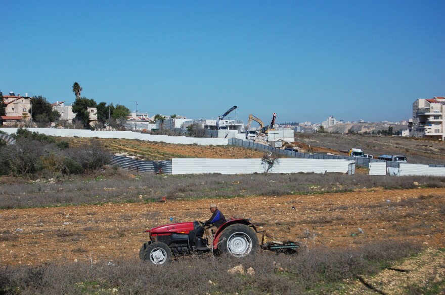 A Palestinian farmer from the nearby village of Jib got an Israeli permit to cross a military checkpoint and prepare his land next to the settlement of Giv'at Ze'ev for sowing wheat. The disputed synagogue is being dismantled in the background as he works.