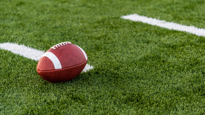 A brown leather american football on a green playing field