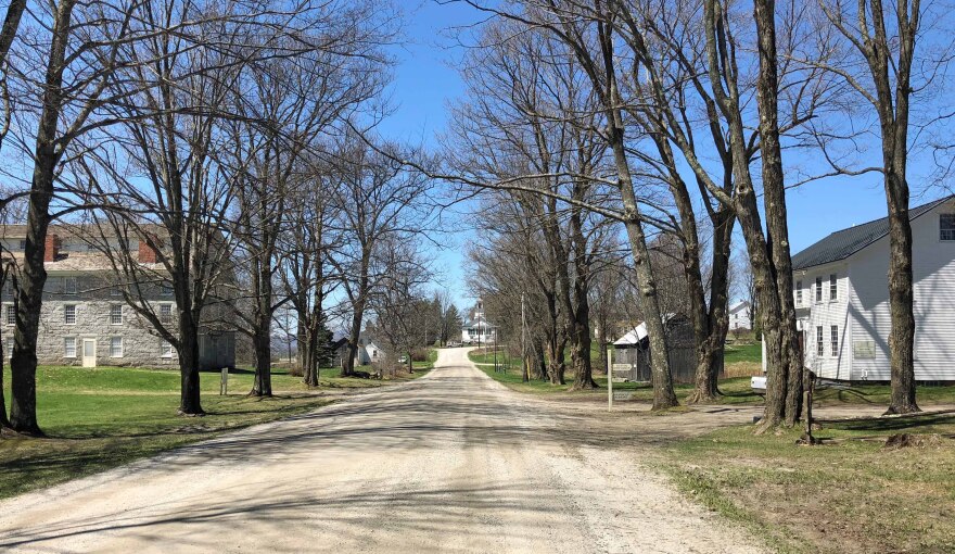 A country road in Brownington on a blue-sky day, the museum spanning both sides of the road.