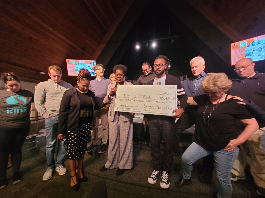 Members of the Sycamore Creek church pray with Justice League of Greater Lansing Founder Willye Bryan and President Prince Solace, standing near each other with their hands on each others' shoulders