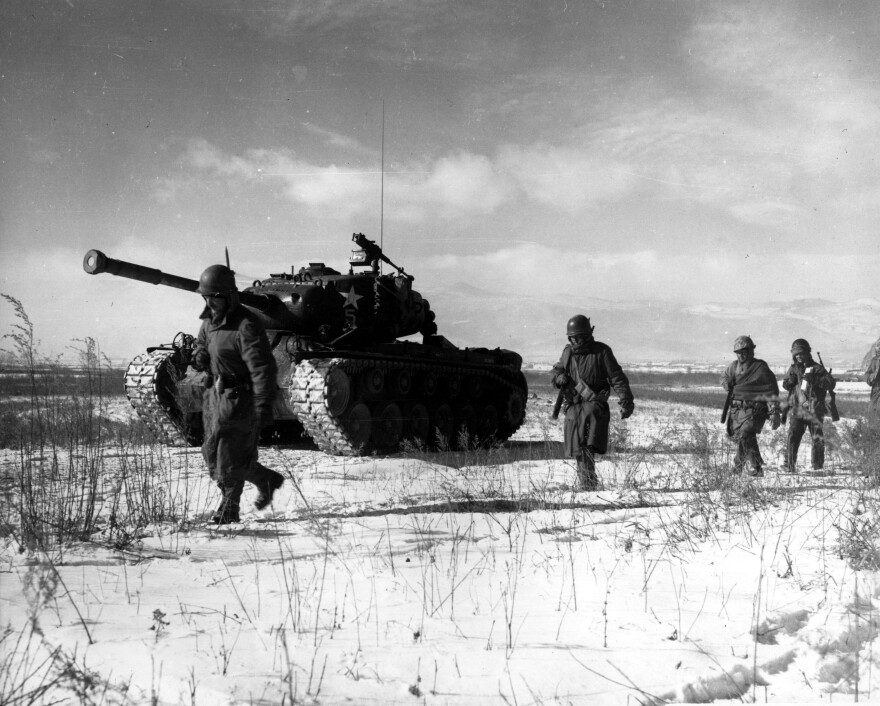 Four US soliders march through the snow next to a tank. 