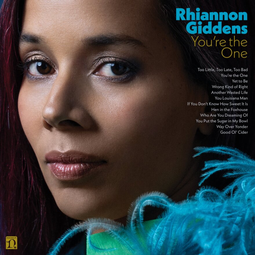 The album art for Rhiannon Giddens' "You're the One" album. Giddens looks into the camera with blue feathers in the bottom left corner. 