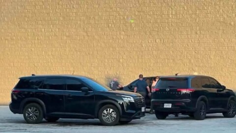  Three black unmarked SUVs parked next to a blank exterior wall with several people standing outside one of them closest to the wall. 