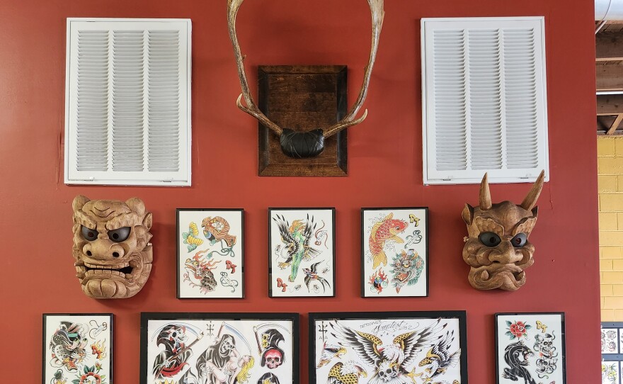 Mounted antlers, face masks, and images of tattoos hang on a wall.