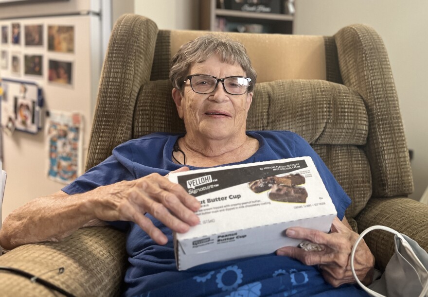 A woman sits in an armchair and holds a box of ice cream peanut butter cup treats. 