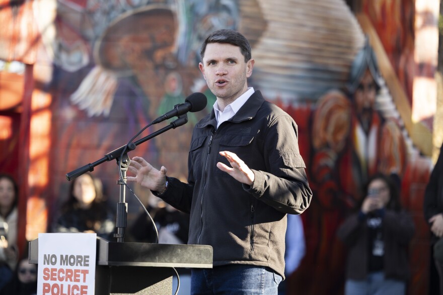 A man gestures as he speaks at a podium during an outdoor rally. 