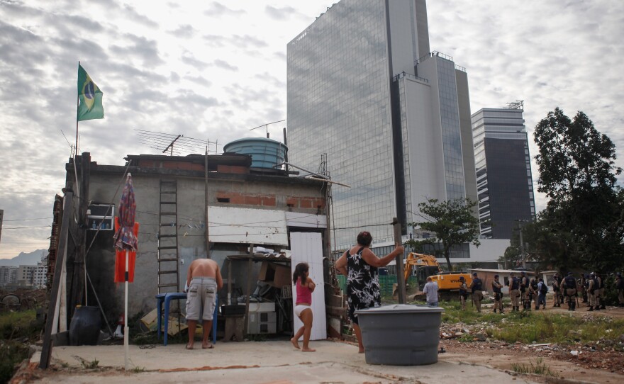 With the Olympics just months away, many wonder whether hosting the Games will be worth the effort. Here, members of the Lopes family watch during the demolition of a building in Rio's Vila Autodromo favela, with new Olympic Park structures in the background, on Feb. 24.