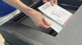 A photo of voters dropping their ballots in to a ballot box