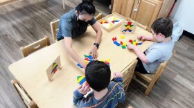 A photo of a woman teaching two children at desk. 