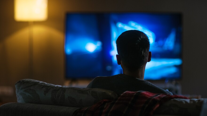 A photo of the back view of a man sitting on a couch watching tv. 