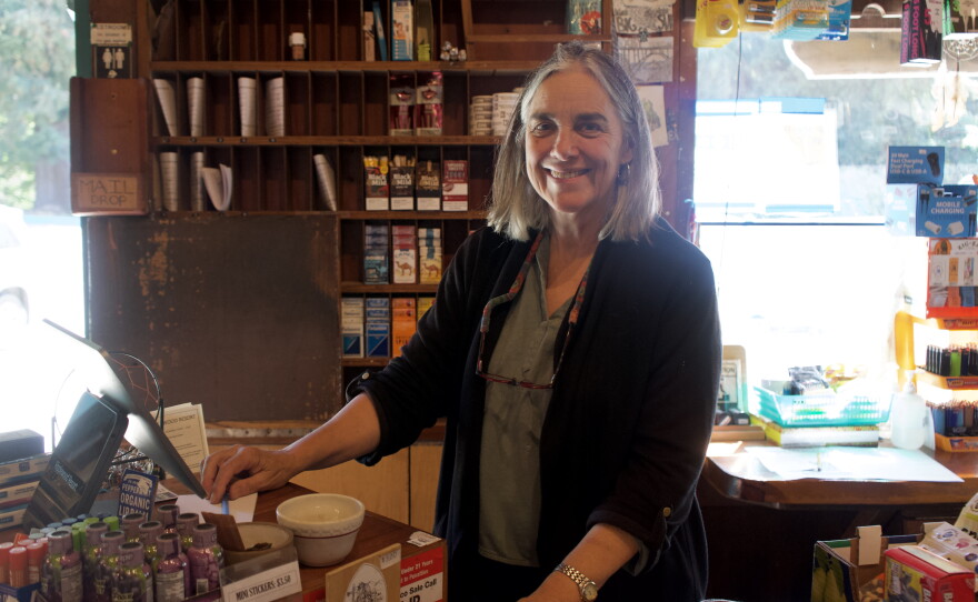 A woman smile and looks at the camera in front of a register. 