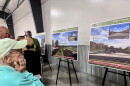 A woman in a blue sweatshirt looks at a sign displaying a rendering of a road with cars on it.