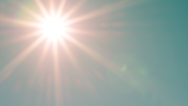  A sun and its rays shine brightly in front of the blue sky.