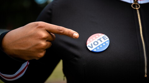 Woman Pointing At A Vote Button Pinned To Her Sweater