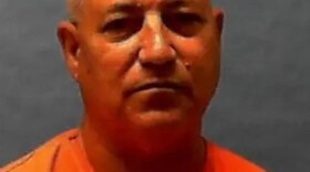 Prison head shot of a white man with balding gray hair in orange prison clothes