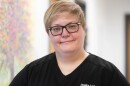 Dr. Jessica Lapinski is a family medicine physician who provides gender-affirming care. She's seen here from the chest up with short strawberry-blonde hair and glasses while smiling directly at the camera.