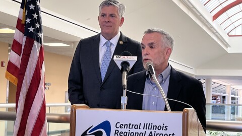 A tall man in a suit with a congressional pin, U.S. Rep. Darin LaHood stands next to a short man, Central Illinois Regional Airport Board Chair Alan Sender, at a lectern with a regional airport placard on the front of the lectern. 