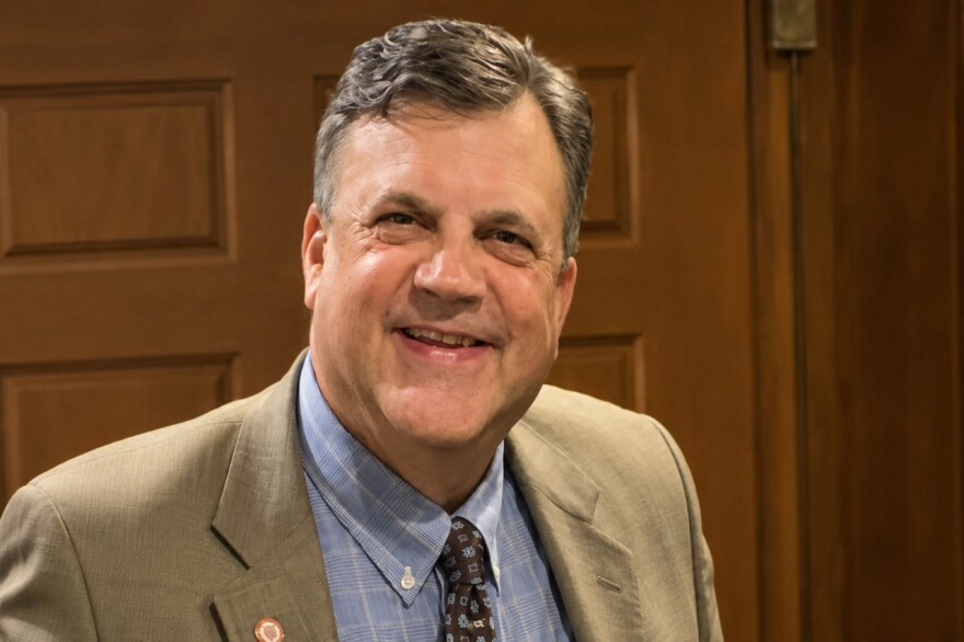 A man smiles at the camera. He's wearing a suit.