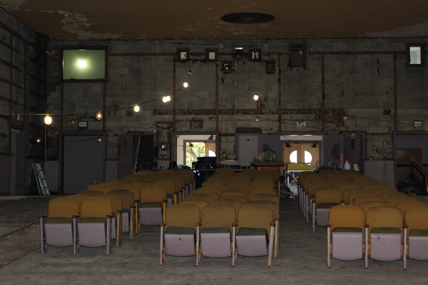 A picture of the view from the stage towards the rest of the theater. Only a few rows of chairs remain. Lights hang from a cord above. 