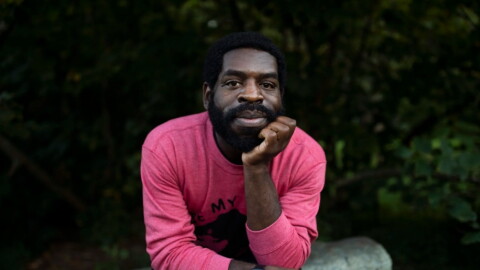 Hanif Abdurraqib sitting a boulder, propping up his chin with his hand