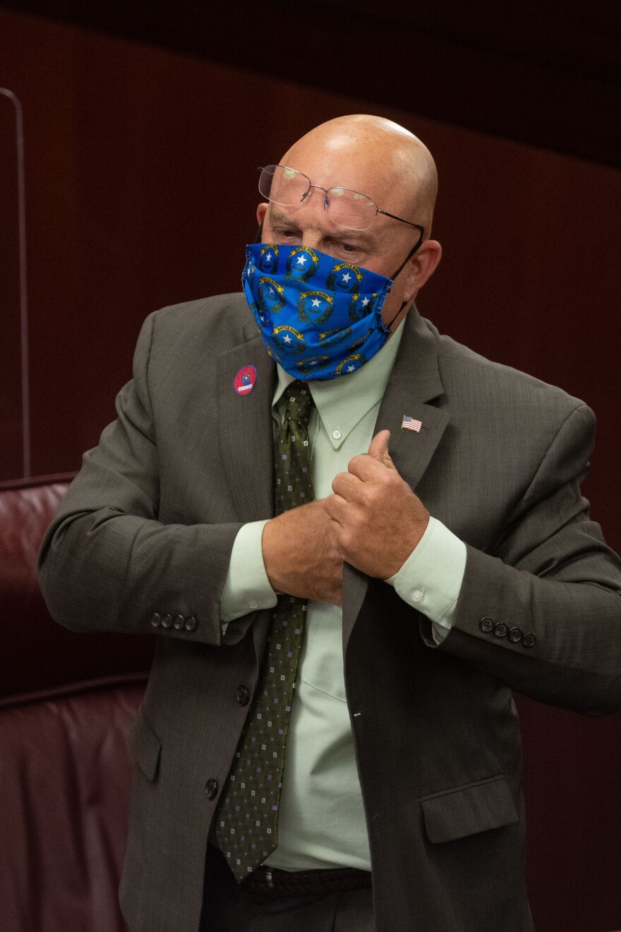 A man wearing a mask is reaching his hand into his suit.