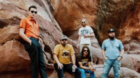 A group of men standing in front of red clay rocks. 