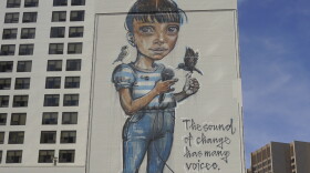 A multistory mural shows a girl holding a microphone, surrounded by birds and birdcages.