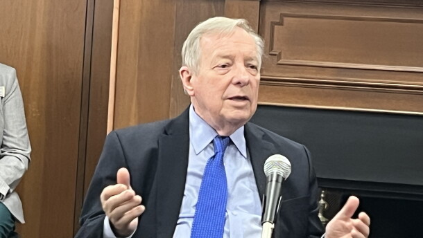 U.S. Senator Dick Durbin sitting at a round table with a microphone on it. His shirt is light blue. His tie is vibrant cerulean. 