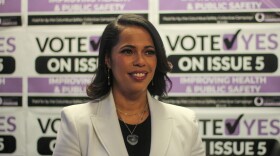 A woman in a white suit smiles in front of a wall of "Vote Yes on Issue 5" campaign signs